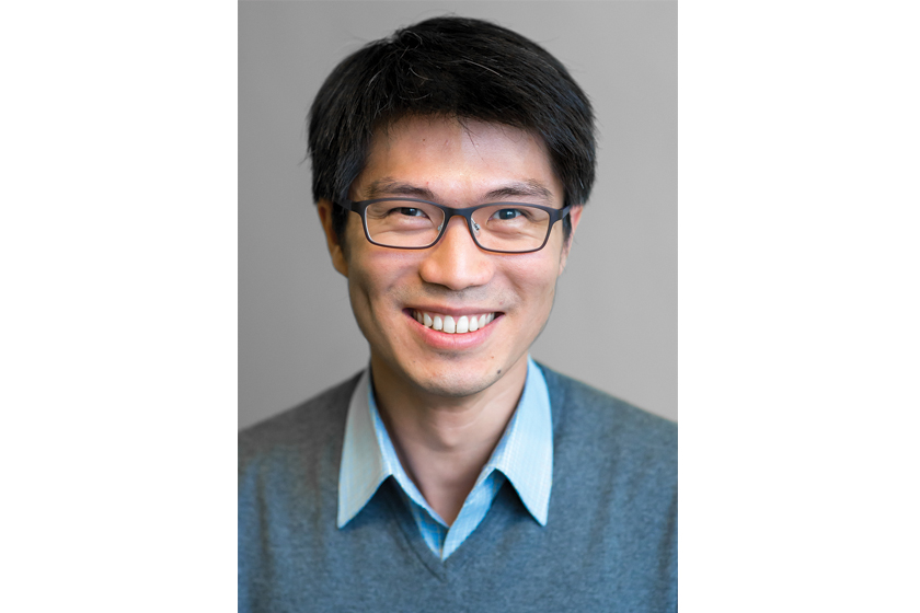 A young man with glasses wearing grey sweater smiling