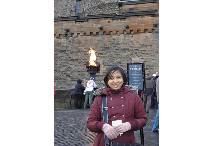 A woman wearing red jacket is standing in front of a castle